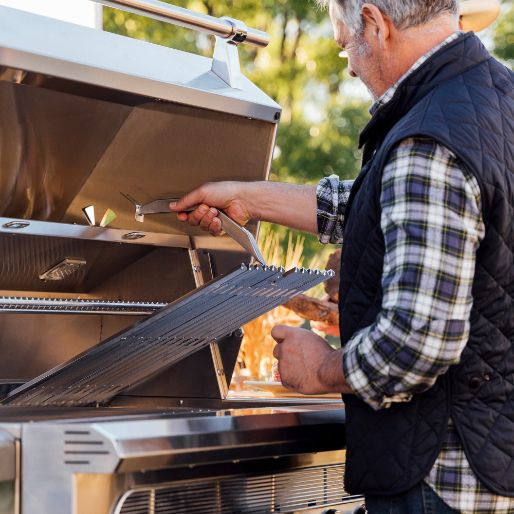 Person using a grate-lifting tool to remove a cooking grate from an American Made Grills Muscle grill