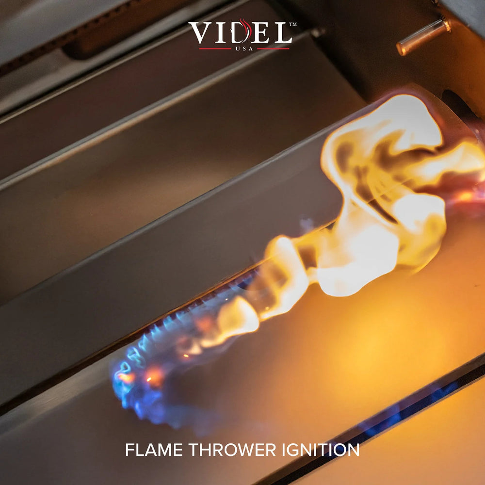 Close-up of a flame thrower ignition with a blue jet of gas igniting into a bright yellow and orange flame inside a metallic device. The VIDEL USA logo is visible at the top, and 'FLAME THROWER IGNITION' is written at the bottom.